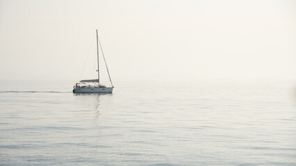 Fototapeta premium Sailboat with mast and open sails sailing on a calm sea on a misty day