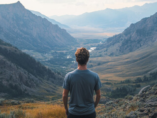 Naklejka premium Man Contemplating Majestic Mountain View: A solitary figure stands on a mountaintop, gazing out at a breathtaking panorama of rolling hills and valleys. The image evokes a sense of awe, tranquility, a