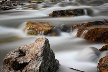 Water flows quickly around rocks in a creek, creating a smooth, silky effect