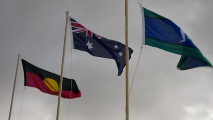 Australian national flag, Aboriginal flag and Torres Strait Islander flag on a windy, overcast day. Clip 3