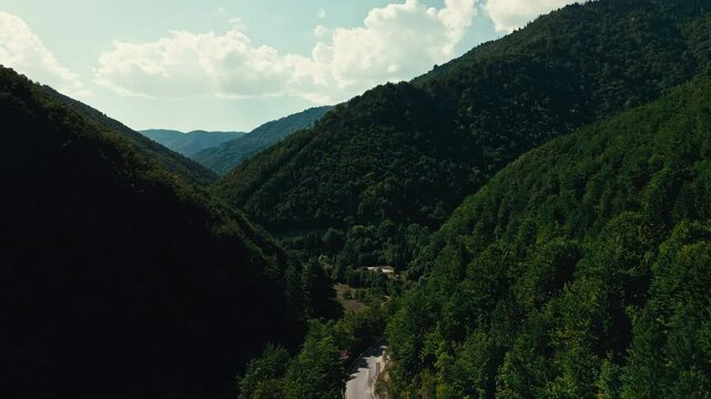 A mountain range with a road running through it in Rogova canyon in Kosovo east Europe. The road is surrounded by trees and the sky is cloudy.