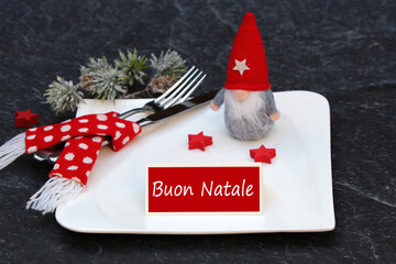 Tavola di Natale apparecchiata festosamente con piatti e posate. Biglietto con il testo Buon Natale.