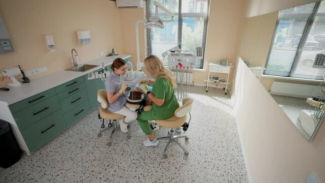 Blonde Woman Dentist with Assistant Treat Teeth of Female Patient with Special Instrument. Treatment of Caries and Plaque in Dental Clinic. Concept of Medicine and Healthcare. Slow Motion.