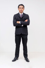 Full-body Portrait of a stoic and serious young asian businessman in a suit and tie, arms crossed...