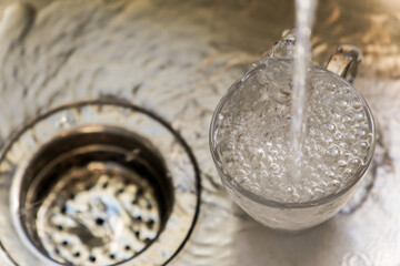 stream of clear water filling a glass tumbler at a kitchen sink