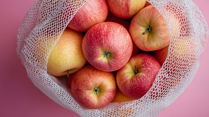 Red apples in beige mesh bag lying on pink surface