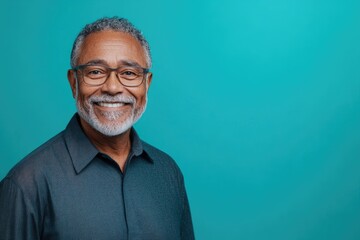 Obraz premium Senior male presenter with a kind smile, standing against a solid turquoise background with ample room for text
