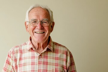 Elderly man in a checked shirt, smiling, standing against a solid cream background with space for messaging