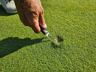 An individual repairing a patch of grass on a golf course during the afternoon using a specialized tool for aeration