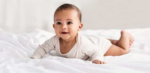 Childcare. Portrait of cute little African American baby wearing bodysuit lying on the white...