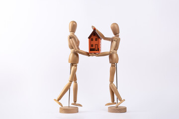 2 wooden figures holding a house. Depiction of a couple who have bought a house, isolated on white background. Copy space. Concept of house and couple