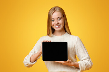 Naklejka premium Digital tablet with black blank screen in young girl's hands, orange backgroung with free space