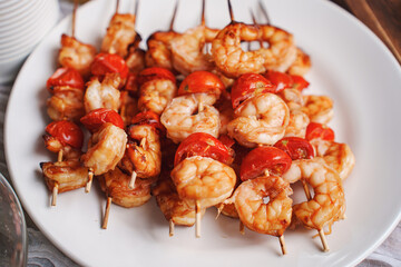 Skewers with shrimps and tomatoes on a white plate. 