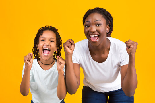 African American Woman And Girl Celebrating Success, Clench Fists And Exclaim With Triumph Over Yellow Background