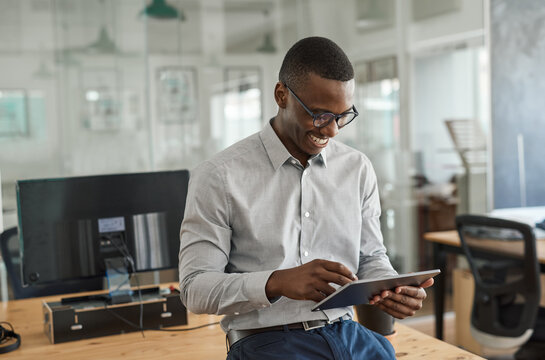 Smiling African businessman leaning on an office desk using a tablet