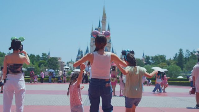Asian mother and adorable kid daughters walking at the theme park. 