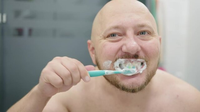 Man brushing his teeth with toothpaste and toothbrush in bathroom, morning routine