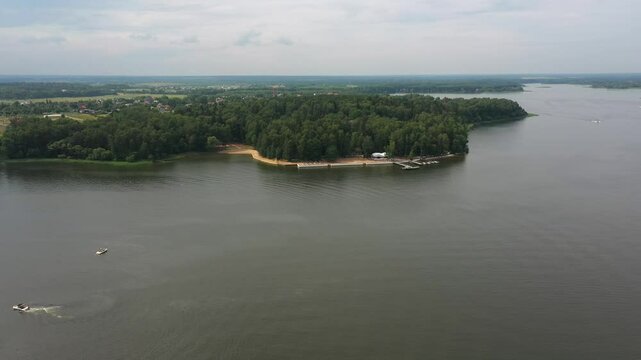 drone flies above wide river on cloudy summer day, boat dock near, wakeboarding