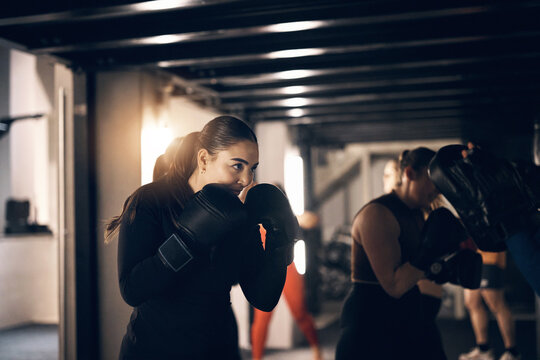 Fit young woman wearing sportswear and boxing gloves focused on a punching workout during a boxing class with others at the gym