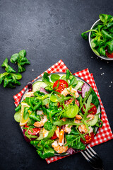 Shrimp salad with tomatoes, lettuce, arugula, cucumber, sesame seeds and lemon dressing on black background, top view