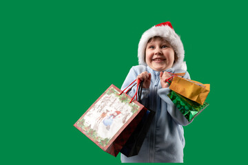 An enthusiastic child wearing a Santa Claus hat with lots of carrier bags with holiday shopping. Png.