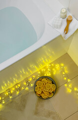 A bowl of lemon slices on the floor illuminated by garlands and a bathtub with turquoise water.