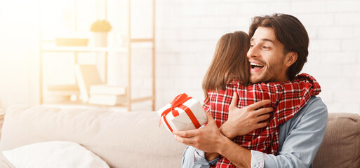 Emotional young father hugging his little daughter, holding gift box at home, free space