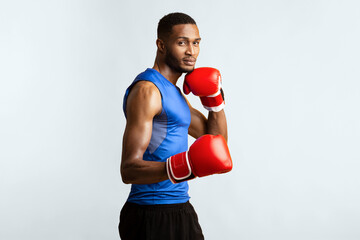 Boxing Stance. Muscular afro sports man in gloves looking at camera, yellow studio background,...