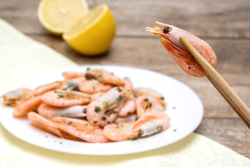 Fresh cooked shrimp on chopsticks, defocused plate with prawns with lemon and spices. Delicious healthy seafood, protein meal.