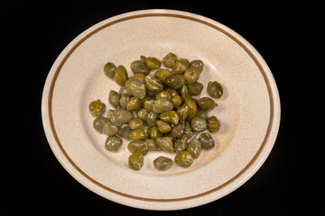 Pickled capers on a saucer on a black background