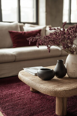 a close-up view of a living room setting with a focus on the textured red rug. The round, black coffee table is adorned with a brown tray, which holds a small vase with branches and two dark bowls