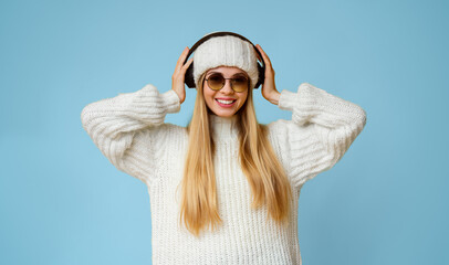 Pretty young winter girl in wireless headphones listening to music, yellow background