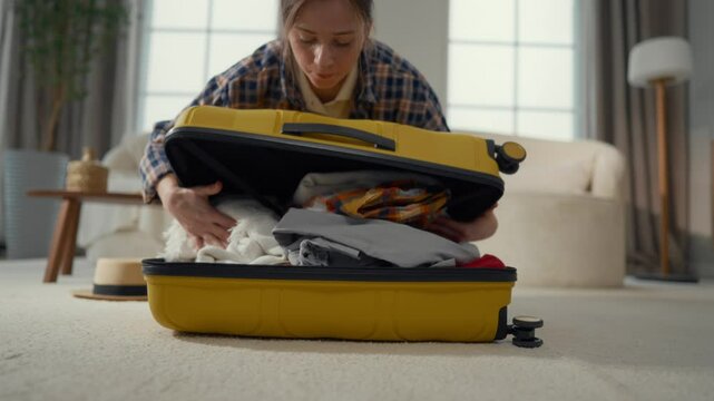 Trip to study or vacation journey, young woman packing suitcase in living room. Happy girl preparing travel bag for airplane flight or ride by train, packing baggage, putting clothes into suitcase