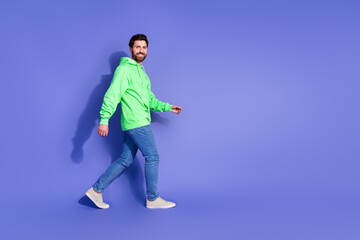 Full length photo of handsome young guy walk profile empty space dressed stylish green garment isolated on violet color background