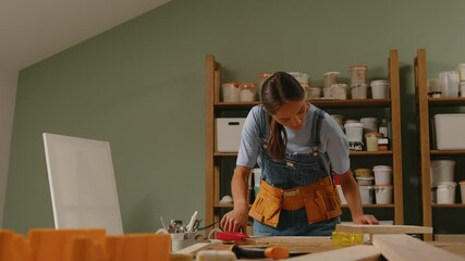 A woman artisan works in her workshop, measuring wood and marking it with a marker for her project. Ideal for showcasing craftsmanship, precision, and woodworking skills.