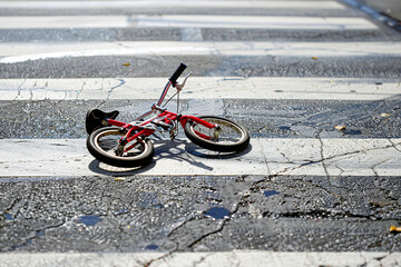 A child's bicycle lies damaged on a crosswalk, depicting the scene of a traffic accident.