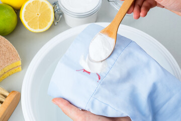 Female hands showing sprinkled with soda baking cosmetic stains on the blue clothes in a plastic basin of cold water. Natural ingredients for green cleaning alternatives. isolated. top view.