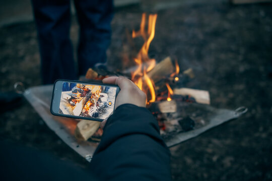 スマートフォンで焚火の写真を撮る手元
