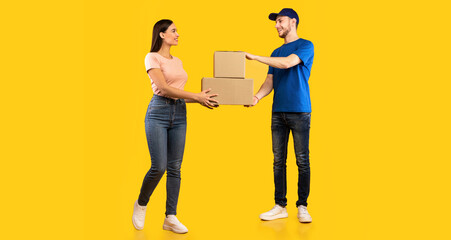Parcel Delivery. Woman Receiving Boxes From Male Courier Standing Over Yellow Studio Background. Post Package Delivering And Transportation, Couriers Service Concept. Full Length
