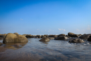 A serene coastal view at El Tunco, El Salvador with smooth rocks in shallow water under a bright blue sky