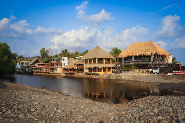 Fototapeta premium Scenic view of El Tunco's riverside cafes against a vibrant sky in El Salvador during early afternoon
