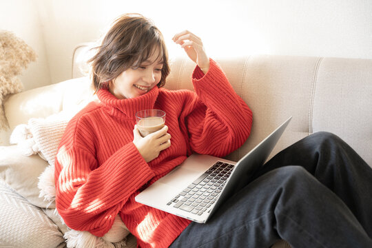 ソファに座って笑顔でパソコンの画面を見ている女性