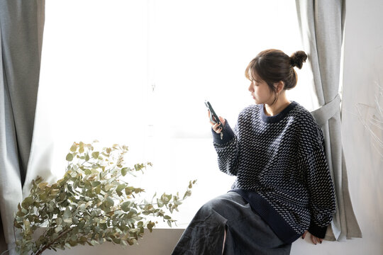 窓際でスマホを見ている女性
