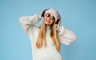 Playful young winter girl in wireless headphones listening to music and dancing, yellow background