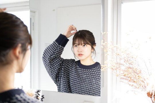 バスルームで鏡を見ながら髪の毛を触っている女性