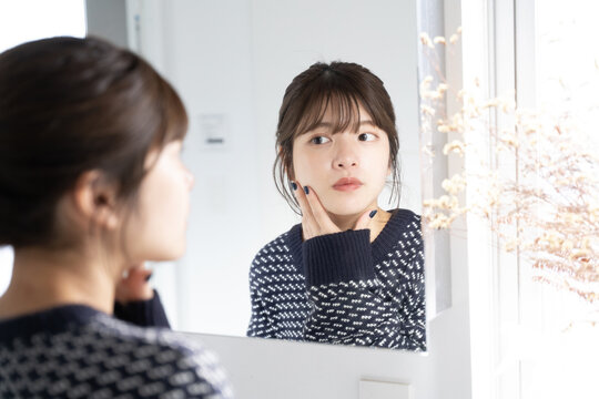 バスルームで鏡を見ながら肌をチェックしている女性
