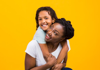 Obraz premium Togetherness Concept. African daughter hugging her mum from the back, showing her love, yellow studio wall
