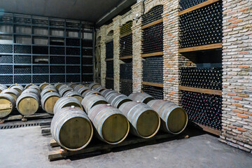 Oak barrels with wine. Brick walls with niches and metal shelves in which bottles of wine are kept.
