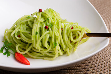Spaghetti pasta with green sauce and red peppers on a fork