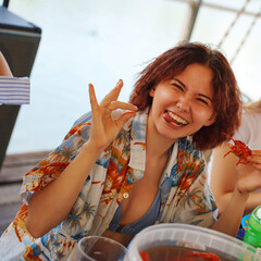 Funny young woman eating boiled crayfish at a party in summer.